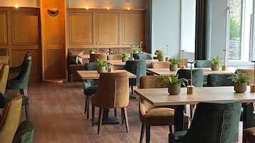 A restaurant with wooden paneling, green upholstered chairs, and potted plants on tables.