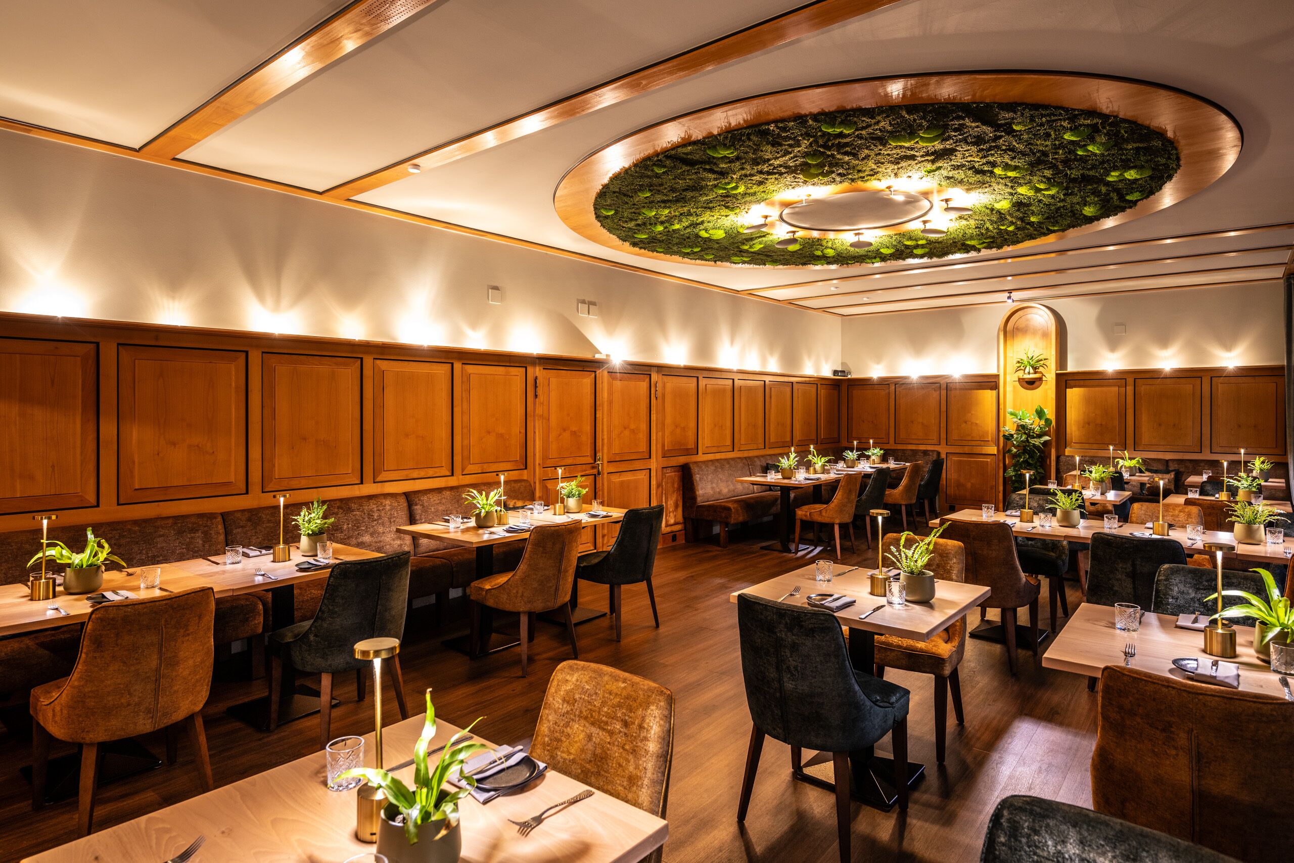 Ein Restaurant mit Holzwänden, mehreren Tischen mit Stühlen und Zimmerpflanzen.