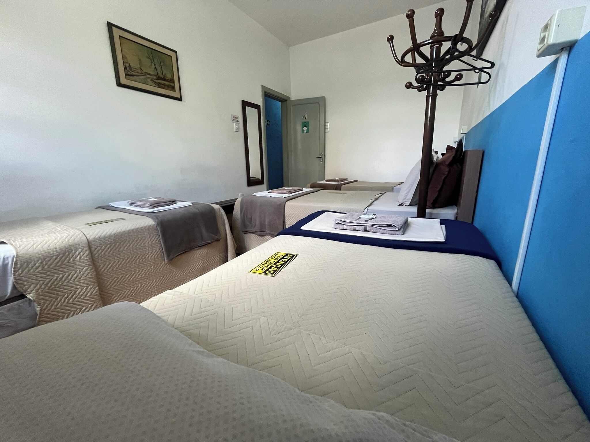 A hotel room with two single beds, a large mirror, a coat rack, and a door to another room.