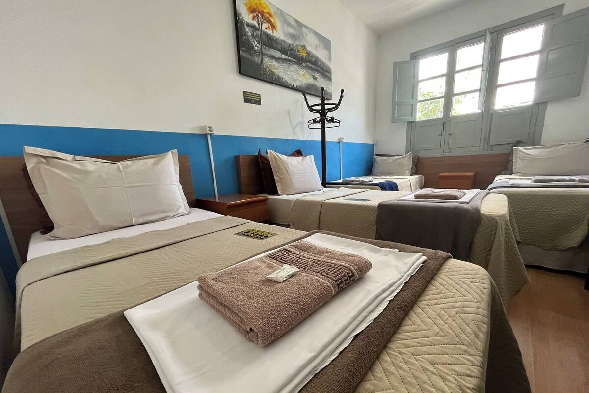 A hotel room with two beds, a painting on the wall, and a window with curtains.