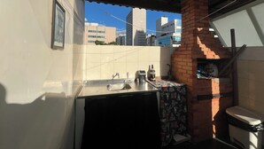 A small kitchen with a sink, a faucet, a tiled backsplash, a brick oven, and a window overlooking a cityscape. - Rota BH Hostel (Belo Horizonte)