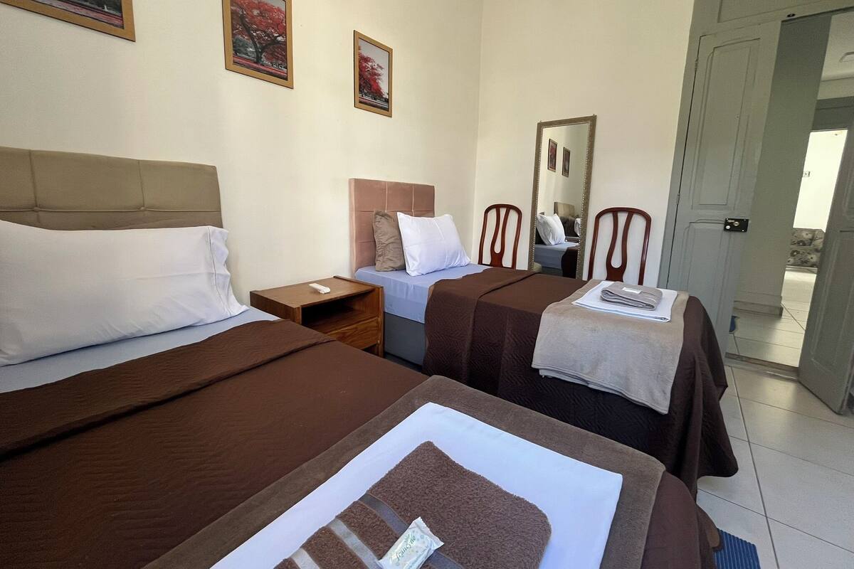 A hotel room with two beds, a nightstand, a mirror, and two framed pictures on the wall.
