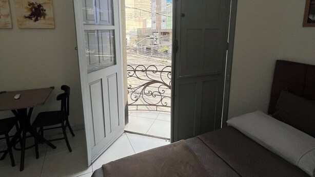 A bedroom with a bed, a desk, and a chair. There is a balcony with a metal railing. - Rota BH Hostel (Belo Horizonte)
