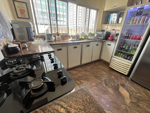 A kitchen with a gas stove, a refrigerator, and a sink. - Rota BH Hostel (Belo Horizonte)