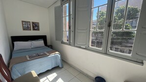 A bedroom with a bed, a window, a wall-mounted picture, and a floor lamp. - Rota BH Hostel (Belo Horizonte)