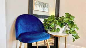 Un fauteuil en velours bleu avec des pieds en bois, une petite table ronde avec un plateau blanc et une plante en pot aux feuilles vertes.