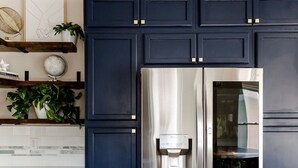 Une cuisine moderne avec des meubles de couleur bleu foncé, un réfrigérateur en acier inoxydable et un plancher en bois.