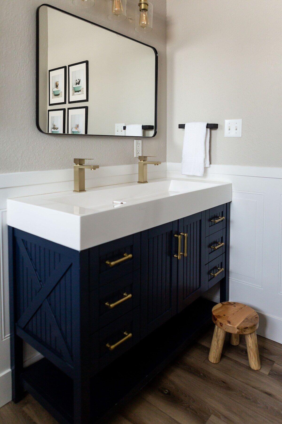 A modern bathroom with a white sink, dark blue cabinets, and a wooden stool.