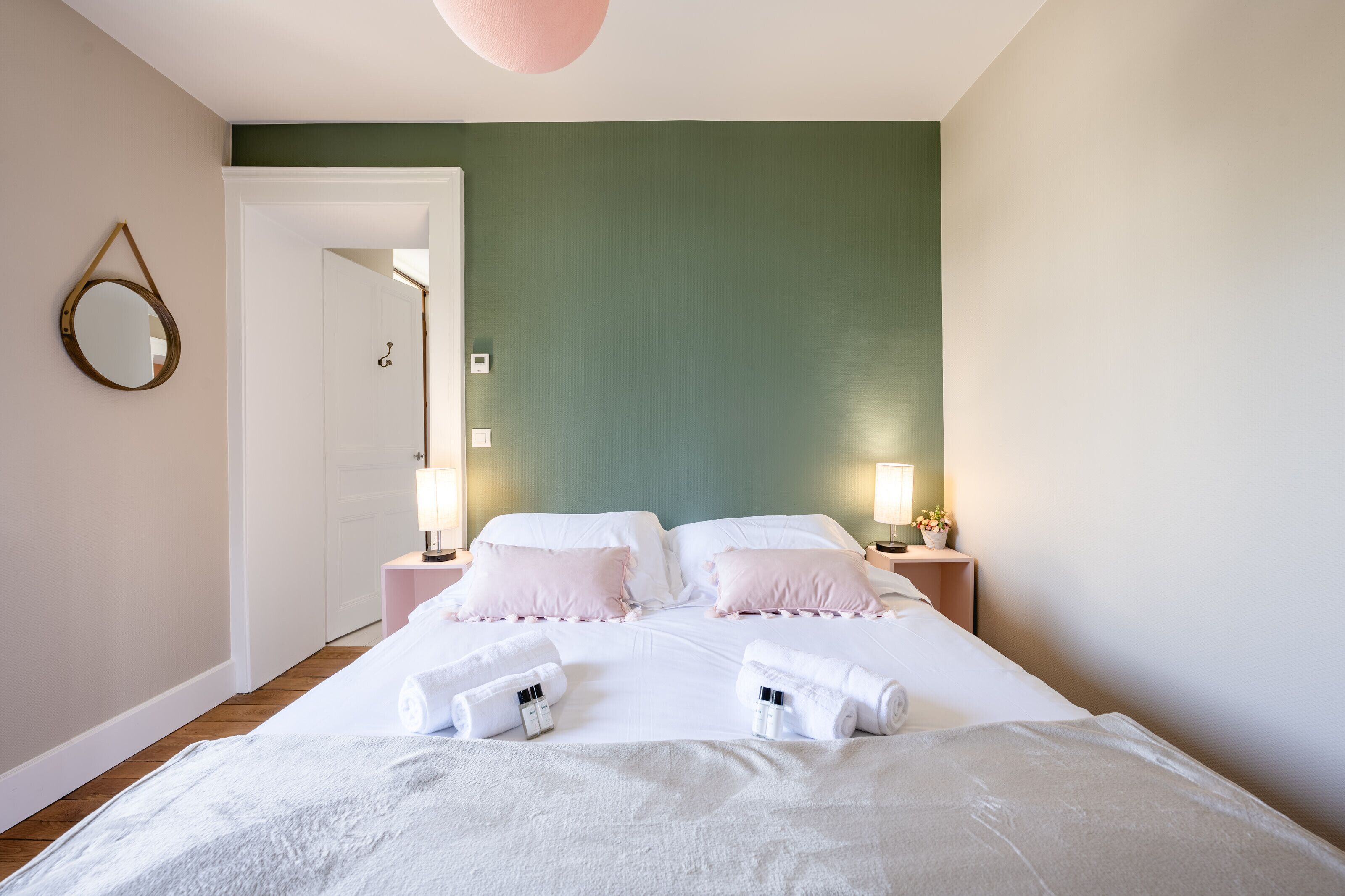 Une chambre d’hôtel avec un lit, deux tables de chevet avec des lampes, un miroir et une porte donnant sur une autre pièce.
