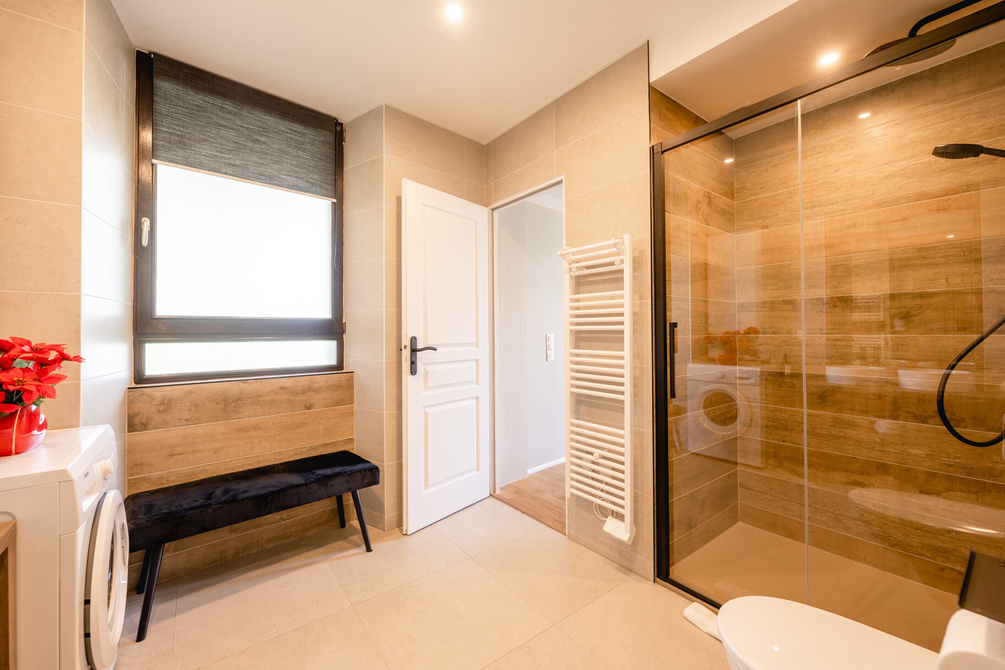 A modern bathroom with a glass shower, a bench, a toilet, and a washing machine.