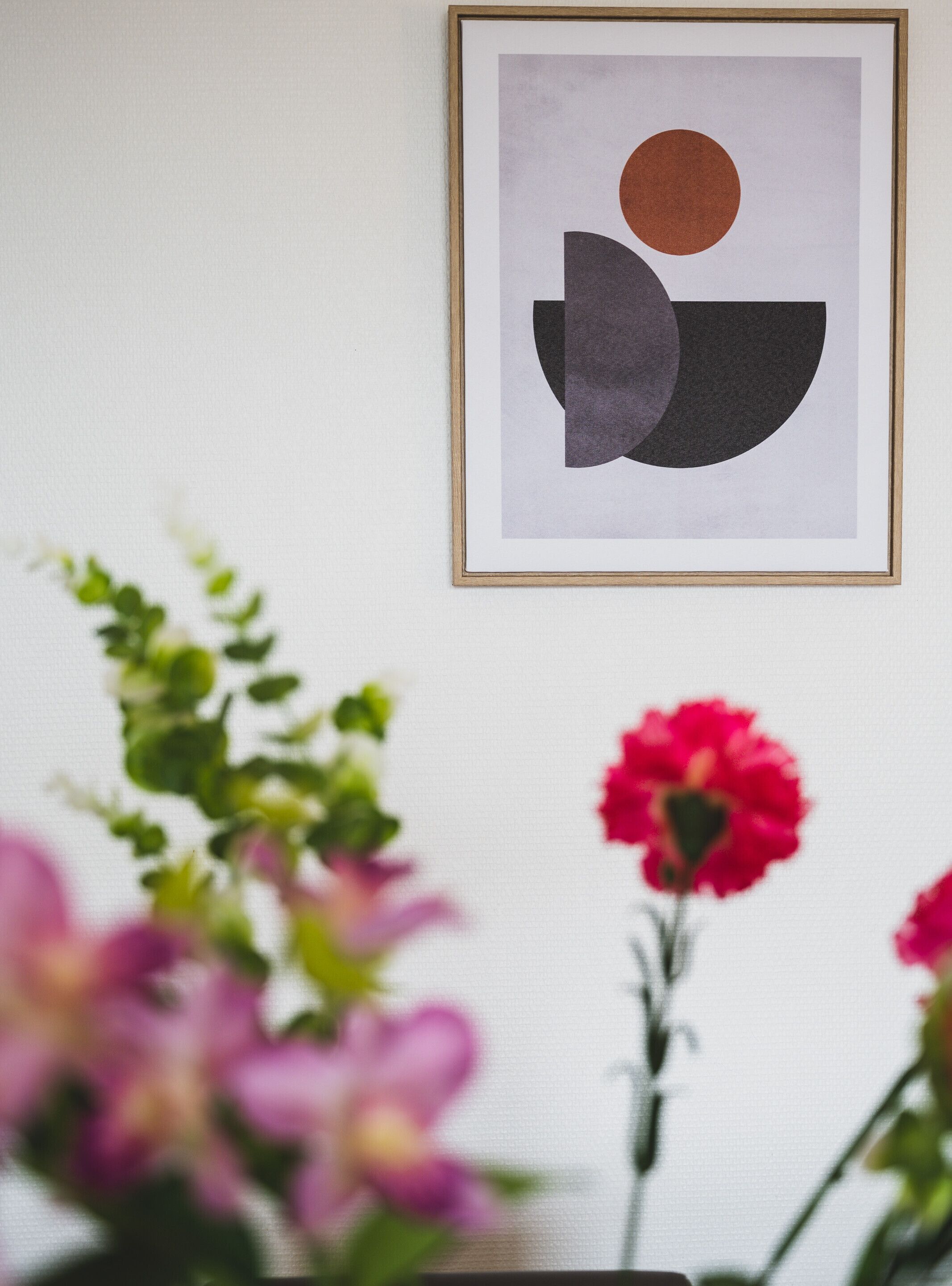 Una obra de arte abstracta enmarcada en una pared, con un primer plano borroso de flores rosadas.
