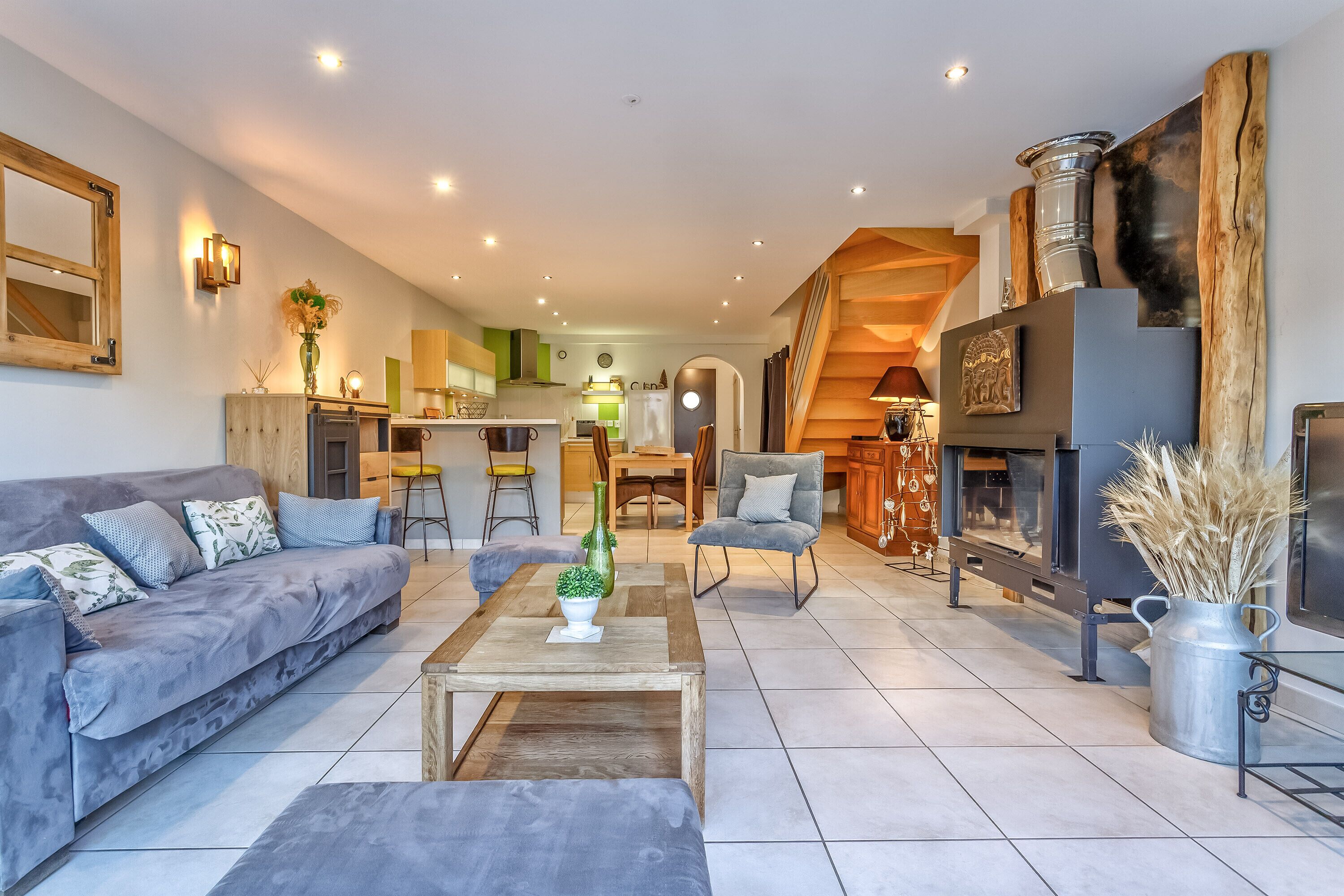 Een moderne woonkamer met een bank, salontafel en decoratieve objecten. In de achtergrond is een keuken met een eethoek zichtbaar.