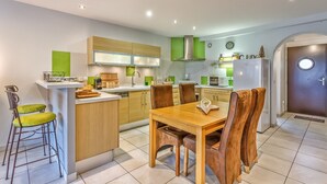 A modern kitchen with a central island, wooden cabinets, and a dining area with a wooden table and chairs. - Les Terrasses de Bredanne (Doussard)