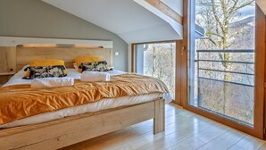 A bedroom with a large bed, wooden headboard, and a view of a balcony with trees. - Les Terrasses de Bredanne (Doussard)