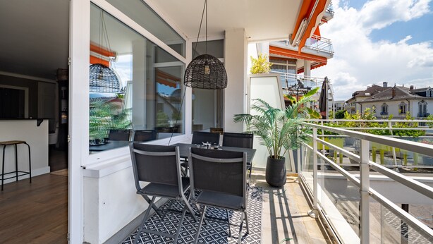 A balcony with a dining area, a hanging light fixture, and a potted plant. - LA MAVÉRIA – Elegant 100 m² flat near Lake Annecy (Annecy-le-Vieux)