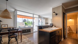 A modern kitchen with a large island, wooden flooring, and a dining area with a table and chairs. - LA MAVÉRIA – Elegant 100 m² flat near Lake Annecy (Annecy-le-Vieux)