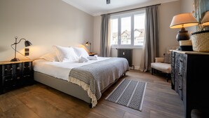 A bedroom with a bed, bedside tables, a dresser, a window with curtains, and a ceiling fan. - LA MAVÉRIA – Elegant 100 m² flat near Lake Annecy (Annecy-le-Vieux)