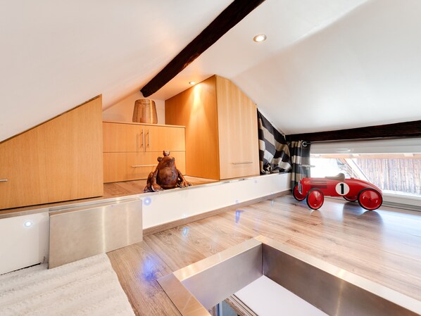 A modern loft bedroom with a sloped ceiling, wooden cabinetry, a large window, and a red vintage car model.