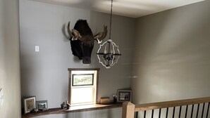 Una stanza con una scala in legno, una testa di bufalo appesa al muro, un lampadario e una finestra che si affaccia sull'esterno.