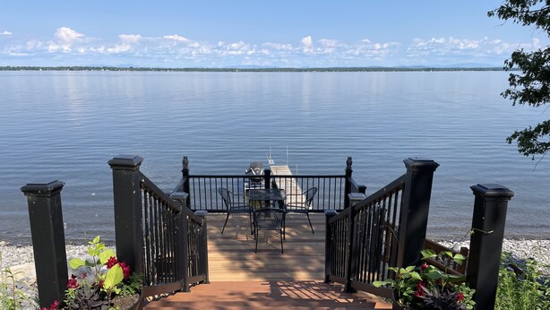 Un pontile in legno con ringhiera, accessibile tramite una terrazza, circondato da piante in vaso.