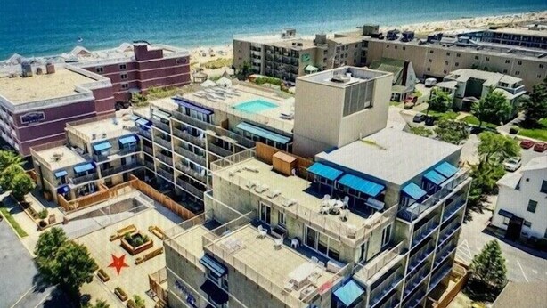 Zona residencial costera con edificios de apartamentos modernos, una piscina y una playa al fondo.