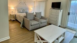 Una sala de estar acogedora con un sofá a rayas, una mesa de centro blanca y un televisor sobre un mueble.