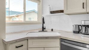 Una cocina con armarios blancos, un grifo negro, una cafetera y un lavavajillas.