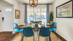Comedor con una mesa de madera dispuesta para cuatro, sillas azules, un tapete tejido y una lámpara colgante.