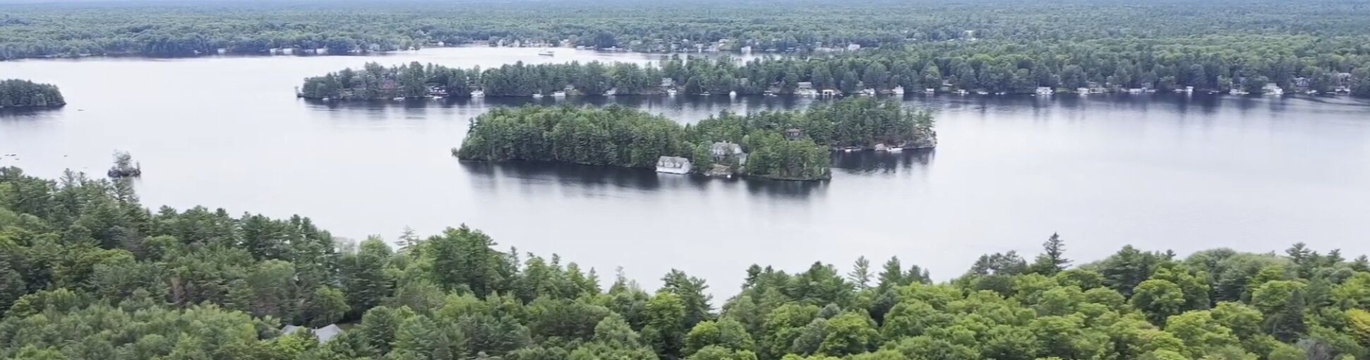 Un lac entouré d’une forêt dense, avec plusieurs petites îles et quelques bâtiments visibles.