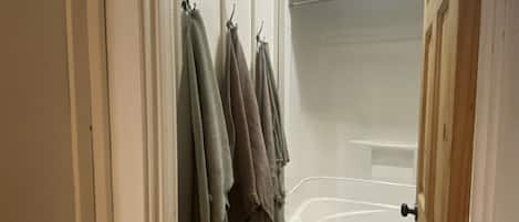 Een badkamer met een bad, een witte deur en een handdoekrek met meerdere handdoeken.
