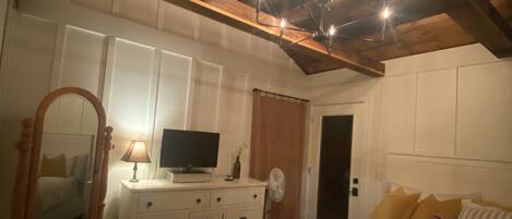 Een slaapkamer met een houten plafond, een bed, een dressoir, een spiegel, een televisie en een deur.