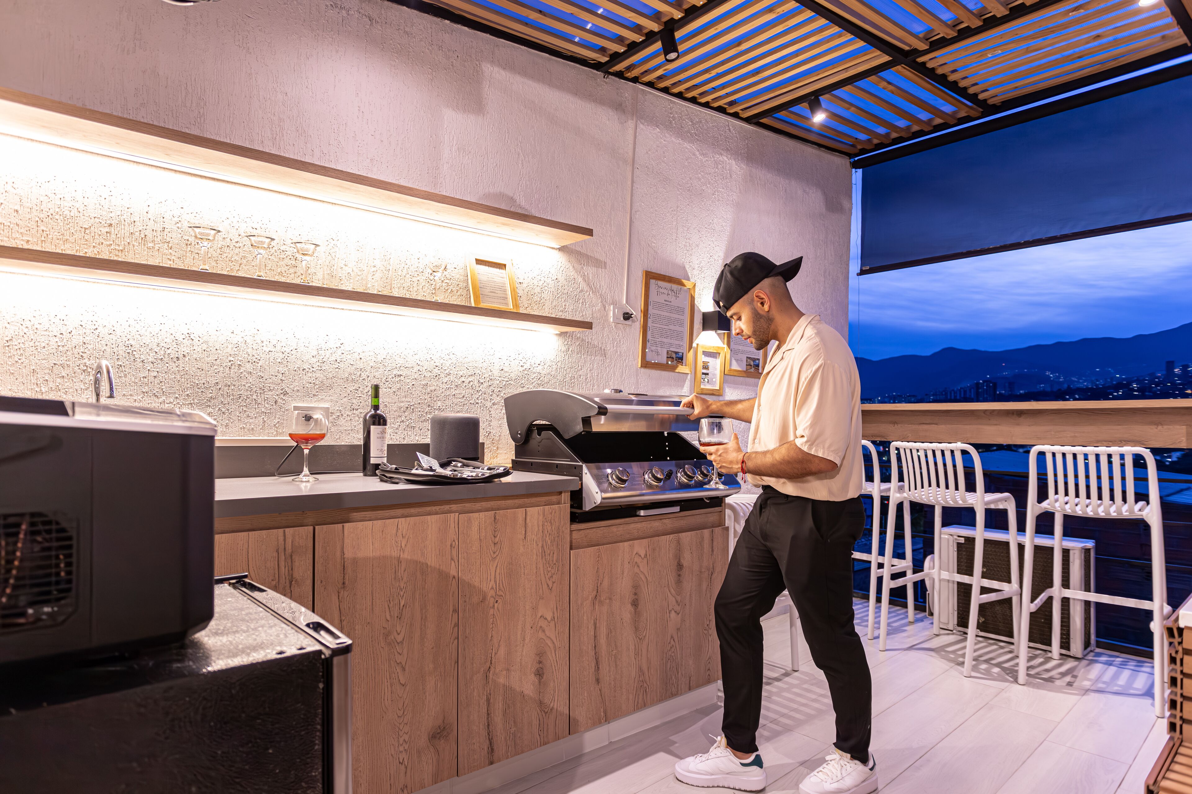 Eine moderne Küche mit Grill, Bar und Sitzgelegenheiten an einem großen Fenster mit Blick auf eine Stadtlandschaft.