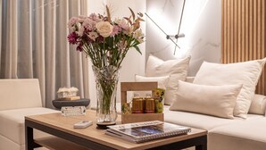 Una sala de estar con una mesa de centro de madera, un florero con flores, una revista y una pequeña caja de bocadillos.
