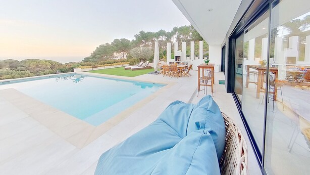 Uma área de piscina moderna ao ar livre, com um espaço de estar envidraçado e vista para a paisagem circundante.