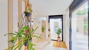 Um interior moderno com uma planta central, uma escultura de madeira e vista através de uma porta de vidro.