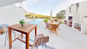 Um pátio externo com piscina, mobiliário de madeira e vista para a paisagem ao redor.