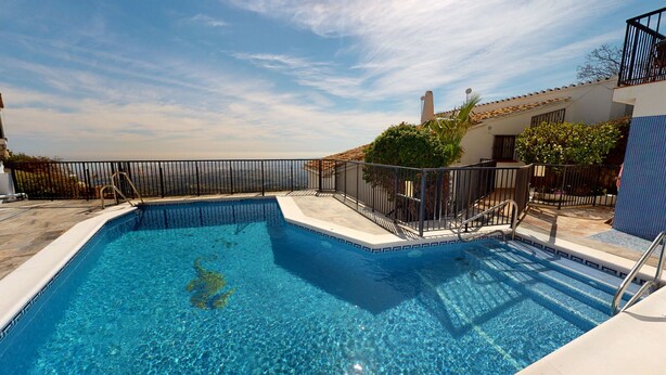 Una piscina rectangular con agua azul cristalina, rodeada por una cerca de metal negro y una zona de solárium con baldosas.