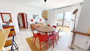 Una sala de estar moderna con una mesa redonda de madera, sillas rojas, una lámpara colgante de ratán y vistas al exterior a través de grandes puertas correderas.