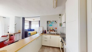 Cocina compacta con armarios blancos, encimera de madera y un lavabo. Hay una zona de comedor con una silla roja y una mesa pequeña.
