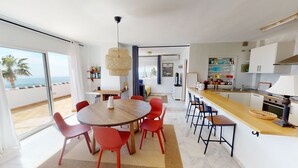 Una cocina moderna con una isla de madera, sillas rojas y un amplio ventanal con vistas al mar.