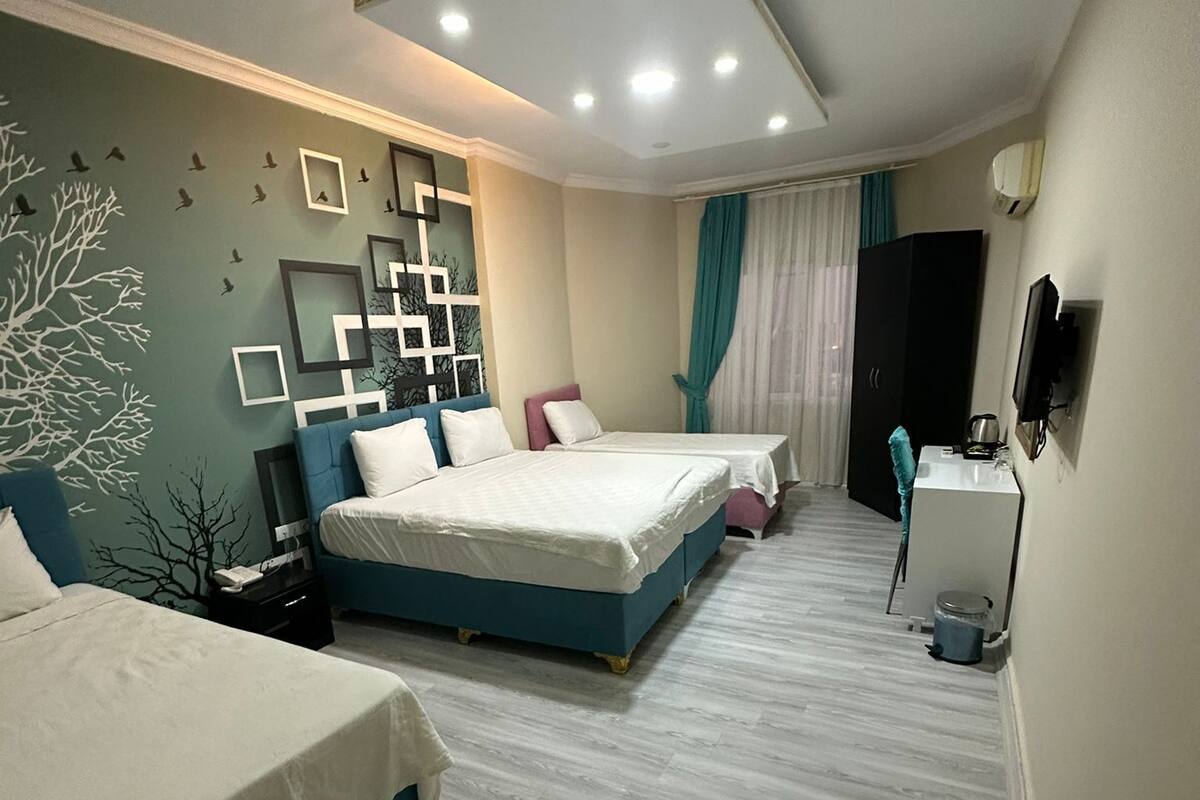 A modern bedroom with two beds, a desk, a TV, and a decorative wall.