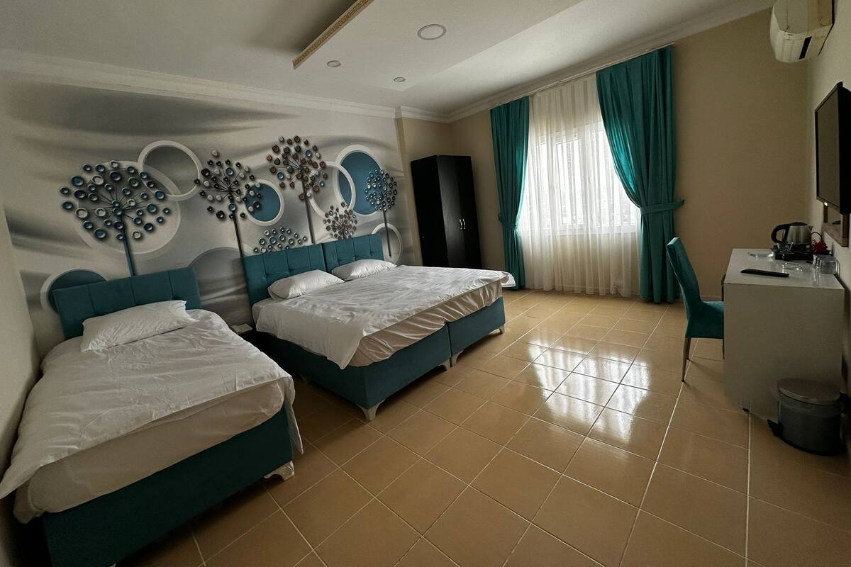 A hotel room with two beds, a desk, a chair, and a large window with curtains.
