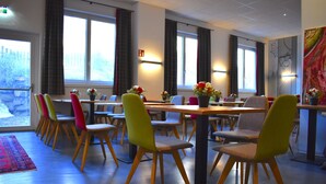 Un comedor con varias mesas y sillas, ventanas amplias con cortinas, y vista al exterior.