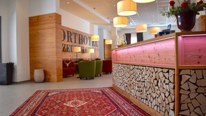 Zona de recepción de un hotel con un mostrador de madera, una alfombra de diseño y una pared con motivos de mosaico.