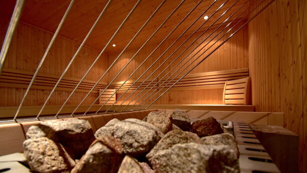 Una sauna con paredes de madera y techo con barras de metal. Se observan rocas grandes en primer plano.