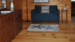Ein Zimmer mit Holzwänden, einem blauen Sofa, einer Holzkommode, einer Lampe und einer gerahmten Karte an der Wand.