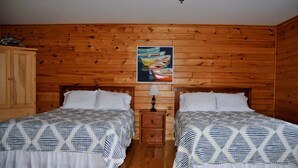 Ein Zimmer mit zwei Betten, Holzwänden, einem Holzschrank und einem Bild von Booten.
