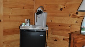 Ein kleines Zimmer mit einem kleinen schwarzen Kühlschrank, einer Kaffeemaschine und einem Mülleimer.