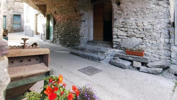 A stone building with an arched entrance, a small outdoor seating area, and a flower bed. - La via del sale  (Pignone)