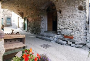A stone building with an arched entrance, a small outdoor seating area, and a flower bed.